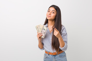 Young arab woman holding dollars pointing with finger at you as if inviting come closer.