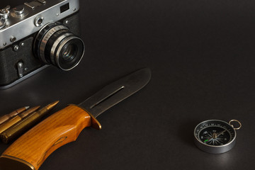Still life with hunting knife, compass, cartridge for a rifle and old analog film camera on black...