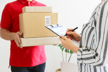 Cropped image of delivery guy in red polo t-shirt handing out the package to young woman. Female receiving the shipment from man wearing shipping company uniform. Background, close up, copy space.