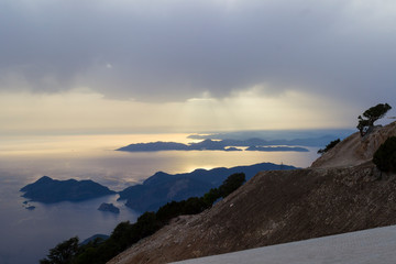 Sunset over the sea, trees on the slopes of the mountains, the sky in clouds