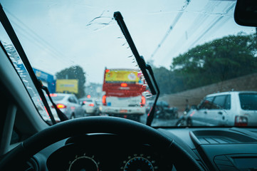 Driving a car in the rain. Inside view, driving on a traffic jam on a cold rainy day. Wet windscreen and wiper cleaning the glass. 