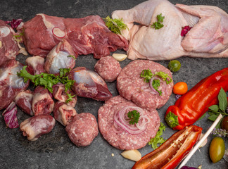 Different types of raw meat: beef, chicken, lamb, gilbert, pork, herbs, lettuce, garlic, cherry tomatoes, bell pepper, greenery