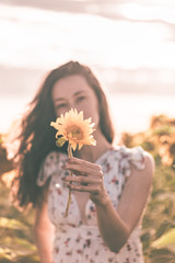 Beautiful lady is walking on sunflower field during the sunset in a summer dress.