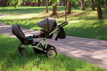 Woman and stroller for twins. A beautiful woman in a park seats two children up to a year in a stroller for twins. Maternity, Modern solutions for twins.