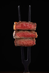 Three beef steak cutout on a fork isolated on black background. Back light contour.