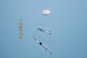 The abbreviation IVF is laid out in wooden letters on a blue background. In vitro injection pen,...