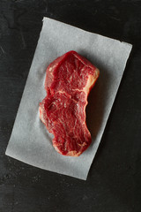 Raw beef meat piece steak with rosemary on black background. Top view, flat lay, place for text.