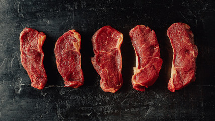 Beef banner. Chopped beef steaks on a black table. Minimal closeup top view flat lay.