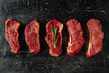 Beef chops background with place for text. Raw beef slices steaks on a dark table with salt