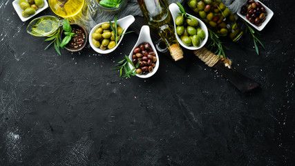 Olive oil, olives and spices on a black stone background. Top view. Free space for your text.