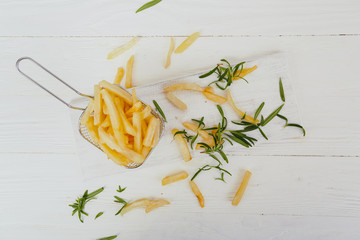 French fries with rosemary on a white wooden table.