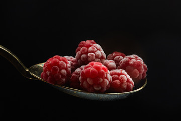 Frozen covered with drizzle raspberry in a bronze spoon isolated on a black background. Raspberry concept.