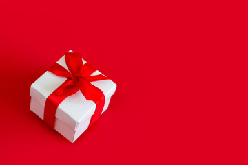 White box with a red ribbon on a red background, copy space. Greeting card concept. Christmas gift