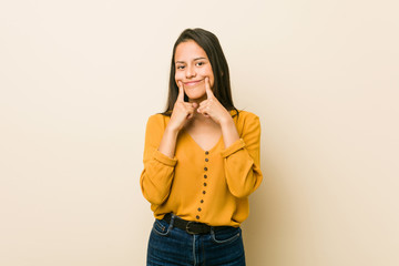 Young hispanic woman against a beige background doubting between two options.