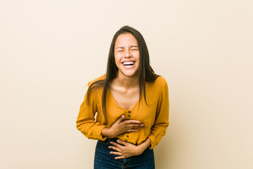 Obraz premium Young hispanic woman against a beige background laughs happily and has fun keeping hands on stomach.