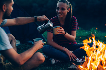 Fototapeta na wymiar happy couple sitting beside camping fire and drinking coffee