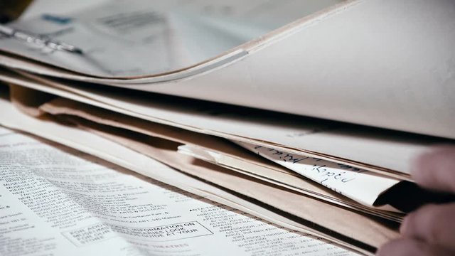 Hands gently searching through old documents and mail for single letter. Close up.
