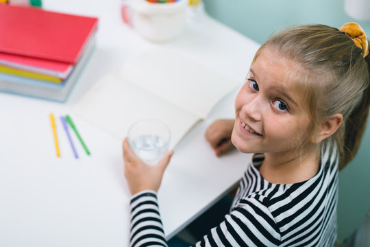 Little School Girl Sitting Desk At Her Room And Drinking Water