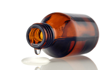 Amber medical bottle with spilled liquid on a white isolated background. Brown glass bottle with liquid close-up