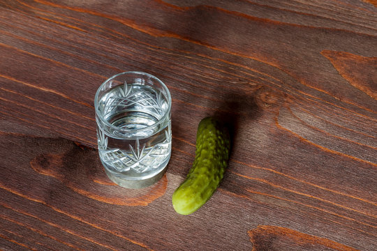 shot of russian vodka and a cucumber close up on a colored brown wooden background. food and drink on a table
