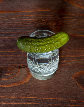  shot of russian vodka and a cucumber close up on a colored brown wooden background. food and drink on a table