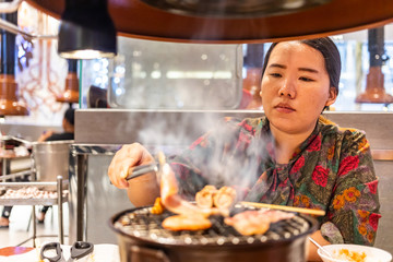 Woman using tongs to grip a piece of grilled meat in restaurant