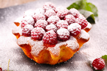 muffin decorated with fresh raspberries on a black plate.