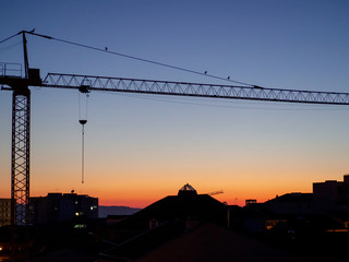 A construction crane over the buildings of a city during sunset.