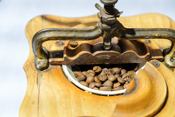 Coffee beans in an old coffee grinder. Old mill for grinding products. Wooden box and metal construction with handle for gear rotation. Roasted, brown, coffee beans in a bowl.