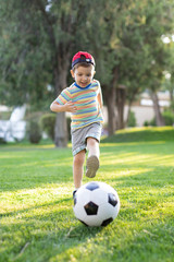 Obraz premium Little boy happy kid playing football and ready to kick the ball on green grass with copyspace