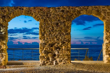 Sunset view of Tyrrhenian sea through stone arch gate in Cefalu, Sicily, Italy