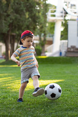 Little boy happy kid playing football and ready to kick the ball on green grass with copyspace