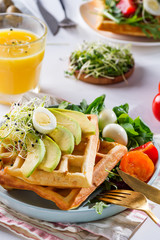 Belgian Waffles with avocado, eggs, micro green and tomatoes with orange juice on marble table. Perfect breakfast for healthy food or lose weight. Avocado sandwich.