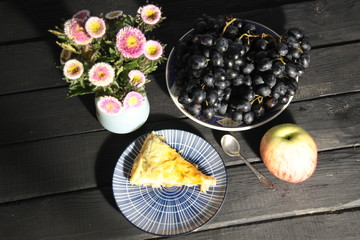 Dessert table with apple pie piecw, black grapes, flowers