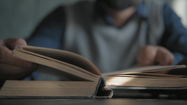 Close-up: the spine of an old book in front of the camera. The man turns the pages and reads a book. Literature. Sun glare on the flyleaf. Reading, education.