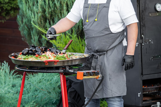 a man cooks pilaf with oysters and shrimp in a cauldron on the street. Cooking. Catering. - Powered by Adobe