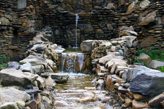 a beautiful mini-waterfall, accompanied by green plants next to it, created by the iridescent pool water