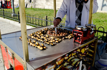 Street vendor selling roasted chestnuts  in tradition street food cart, close up on sunny day, street of Istanbul