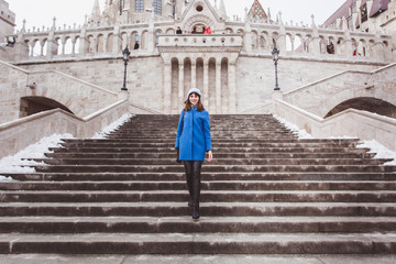 A tourist woman in trendy blue coat stands on the stairs of the Fisherman's Bastion in the Castle...