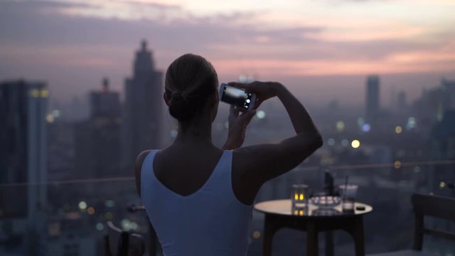 Young woman taking photo of amazing sunset over city