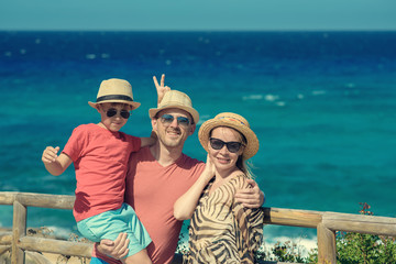 European family spending their vacations by the sea, they are happy together, smiling and looking towards camera.