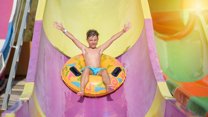 Happy boy on water slide in a swimming pool having fun during summer vacation in beautiful aqua...