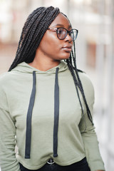 City portrait of positive young dark skinned female wearing green hoody and eyeglasses.