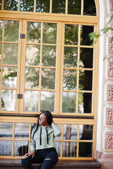 City portrait of positive young dark skinned female wearing green hoody and eyeglasses.