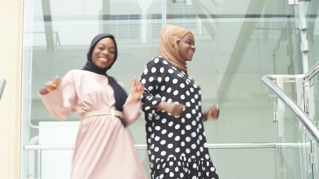 Two positive muslim young women dancing on the stairs in modern business center.