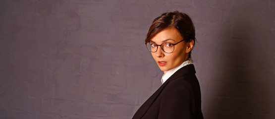 Fashion portrait of a young woman with glasses against a dark wall.