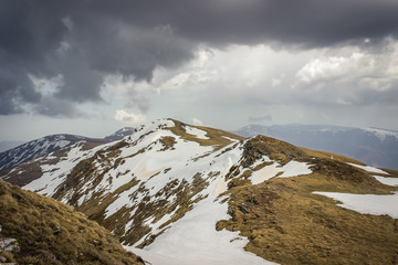 Dramatic, moody view from a Midzor summit, the highest peak of Old mountain, during transition period between winter and spring with some remaining snow and sunlit highlands