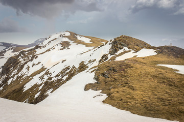 Dramatic, moody view from a Midzor summit, the highest peak of Old mountain, during transition period between winter and spring with some remaining snow and sunlit highlands