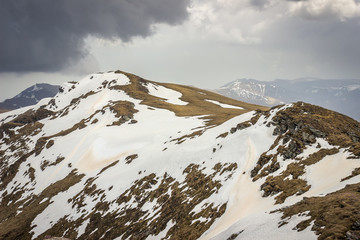 Dramatic, moody view from a Midzor summit, the highest peak of Old mountain, during transition period between winter and spring with some remaining snow and sunlit highlands