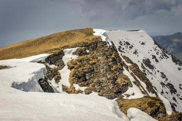 Dramatic, moody view from a Midzor summit, the highest peak of Old mountain, during transition period between winter and spring with some remaining snow and sunlit highlands